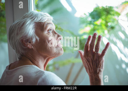 Ältere Frau, die auf der Suche durch Haus Fenster Stockfoto