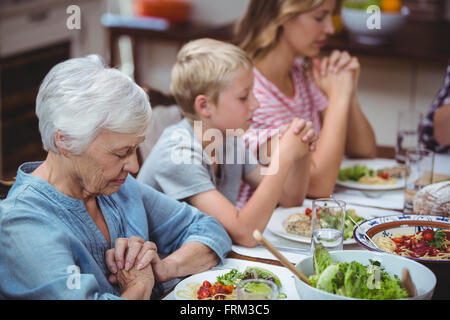 Multi-Generationen-Familie mit Oma am Esstisch sitzen beten Stockfoto