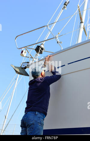 Der Bootsbesitzer poliert zu Beginn der Segelsaison den Rumpf seines Bootes an Land im Jachthafen - Chichester, West Sussex, England, Großbritannien Stockfoto