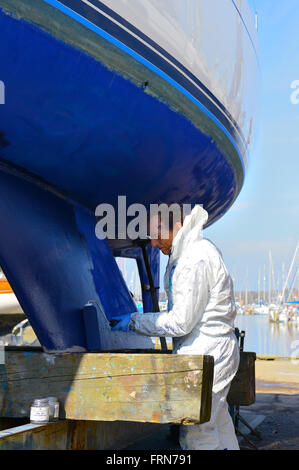 Der Bootsbesitzer, der seine zweikegelige Yacht mit einer Walze (Seewegenprägung) abkeucht und sich auf die neue Segelsaison vorbereitet. West Sussex, Großbritannien Stockfoto