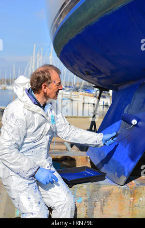 Der Bootsbesitzer, der seine zweikegelige Yacht mit einer Walze (Seewegenprägung) abkeucht und sich auf die neue Segelsaison vorbereitet. West Sussex, Großbritannien Stockfoto