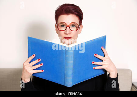 rothaarige Frau mit Brille in ein blaues Buch lesen Stockfoto