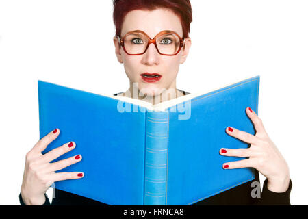 rothaarige Frau mit Brille in ein blaues Buch lesen und schauen überrascht Stockfoto