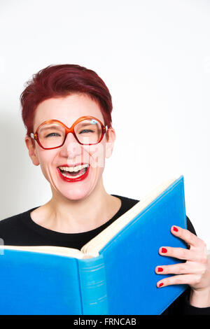 rothaarige Frau mit Brille lesen in ein blaues Buch und lacht Stockfoto