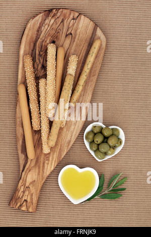 Vorspeise-snack mit Brot-Sticks auf einem Oliven Holz Board mit grünen Oliven und Öl in herzförmige Schalen mit Blatt-Zweig. Stockfoto