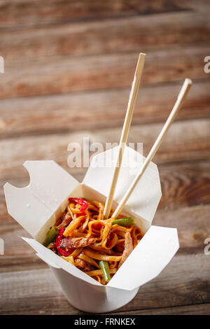 Nudeln mit Schweinefleisch und Gemüse in Take-out Box auf Holztisch Stockfoto