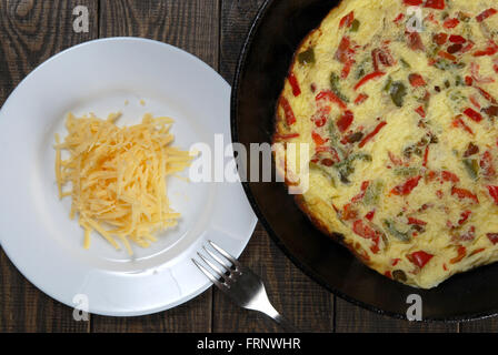 Omelette mit Scheiben von roten und grünen Paprika in die Pfanne mit geriebenem Käse auf einem weißen Teller auf einem Holztisch Stockfoto