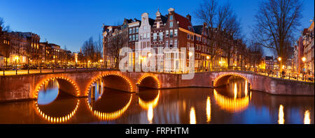 Brücken über eine Kreuzung der Kanäle in der Stadt Amsterdam, die Niederlande in der Nacht. Stockfoto