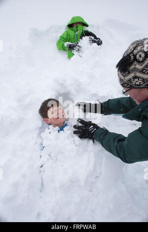 Denver, Colorado, USA. 23. März 2016. VANESSA FINK begräbt JACK FINK, 9 im Schnee, wie IAN FINK, 8, oben ruht, während sie eine vom Schaufeln Pause. Starke Winde und schwere verschneite Großraum Denver im Frühjahr Blizzard heute. Bildnachweis: Matthew Staver/ZUMA Draht/Alamy Live-Nachrichten Stockfoto