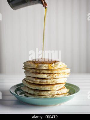 Ahorn-Sirup über einen hohen Stapel von Pfannkuchen gegossen wird. Stockfoto