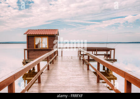 Alte hölzerne Pier für Angeln, kleines Haus Schuppen und schönen See oder Fluss im Hintergrund. Malerische Naturlandschaft. Urlaub Stockfoto