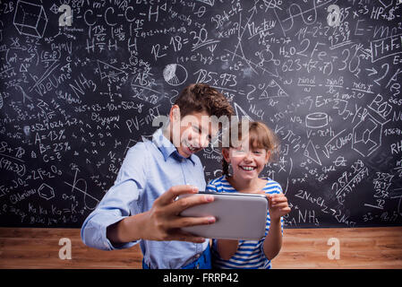 Jungen und Mädchen mit Smartphone, wobei Selfie gegen Tafel Stockfoto