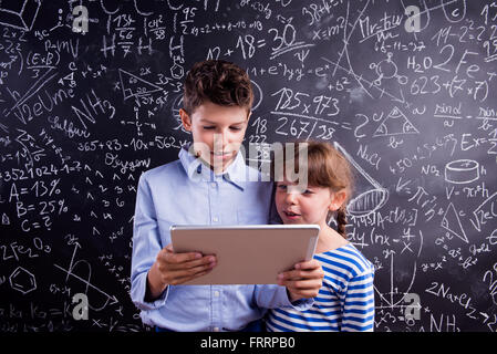 Jungen und Mädchen mit Tablette gegen große Tafel, Schule Stockfoto