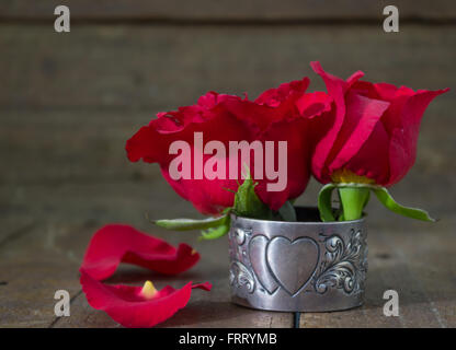 Schmale Tiefe von Feld Schuss aus roten Rosen auf rustikalen Holz in antikem Silber Herz Serviette Halterung Stockfoto