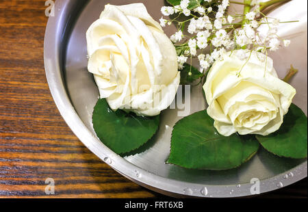 Auf der Oberfläche des Wassers im Behälter ist eine schöne weiße Rosen und kleinen weißen Blüten. Stockfoto