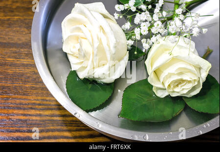 Auf der Oberfläche des Wassers im Behälter ist eine schöne Orange-gelbe Rosen und kleinen weißen Blüten. Stockfoto