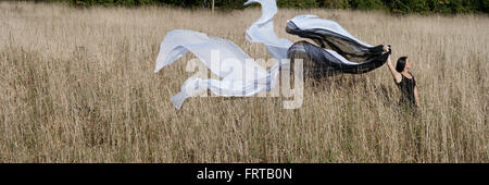 Eine junge Dame in einem schwarzen Kleid läuft auf einem Feld, lange Stoffe fließen hinter ihr. Stockfoto