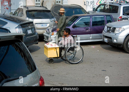 Ein behinderter Mann im Rollstuhl in Armut lebenden verkauft zeremonielle Blumen auf einer Stadt Straße in Penh, Kambodscha. Stockfoto