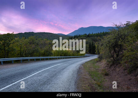 Berg, kurvenreiche Straße, die durch den Wald mit bunten Himmel bei Sonnenuntergang im Sommer Stockfoto