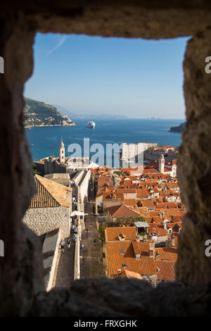 Blick durch eine Fensteröffnung von der Minceta-Turm an der Stadtmauer über die alte Stadt Dächer mit Kreuzfahrtschiff MV Silver Spirit in der Ferne, Dubrovnik, Dubrovnik-Neretva, Kroatien Stockfoto