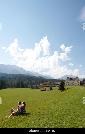 Paar sitzt auf einer Wiese, Kranzbach Burg im Hintergrund, Klais, Krun, Oberbayern, Deutschland Stockfoto