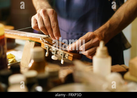 Laute Hersteller Shop und klassische Musikinstrumente: junge Erwachsene Handwerker reparieren alte Konzertgitarre hinzufügen eine Schnur und tuning der Instrumente Stockfoto