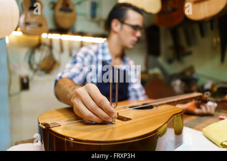 Laute Hersteller Shop und klassische Musikinstrumente: junge Erwachsene Handwerker reparieren alte klassische Gitarre, das Instrument mit einem Metall-tuning Stockfoto