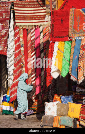 Frau vor einem Geschäft mit bunten Teppichen in den Souks von Marrakesch, Marokko Stockfoto