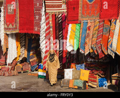 Frau vor einem Geschäft mit bunten Teppichen in den Souks von Marrakesch, Marokko Stockfoto