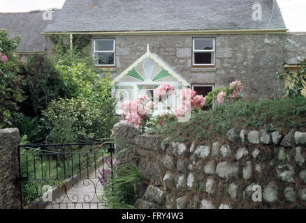 Rosa Rosen neben Wand mit schmiedeeisernen Tor vor der eine Steinhütte mit viktorianischen Glas Veranda Garten Stockfoto
