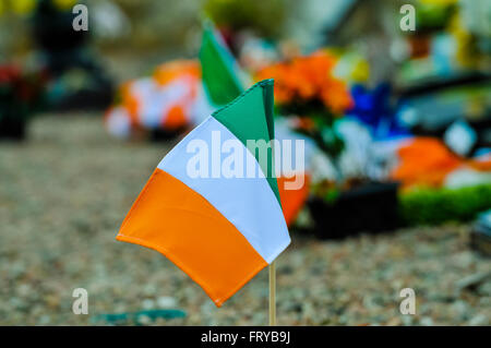 Irische dreifarbige Flaggen und Blumen, die auf einem irischen republikanischen Grabwerk in Belfast hinterlassen wurden Stockfoto