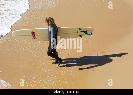 Bournemouth, Dorset, UK 25. März 2016. Surfer und Schatten zu Fuß in Richtung Meer holding Surfbrett am Strand von Bournemouth an einem herrlich warmen sonnigen Tag am Anfang der langen Bank Ostern. Bildnachweis: Carolyn Jenkins/Alamy Live-Nachrichten Stockfoto