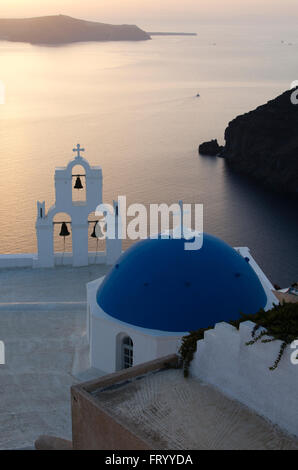 Ausblick auf eine typische Kirche in weiß und blau und die Caldera bei Sonnenuntergang auf der Insel Santorini-Griechenland Stockfoto