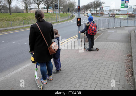 Mutter wartet an der Fußgängerüberfahrt Ampel auf die Straße mit Kindern und Roller zu Fuß zur Schule in Cardiff Wales UK KATHY DEWITT Stockfoto