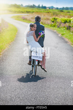 Ein Brautpaar nimmt die Straße auf einem Fahrrad. Sie haben Spaß für ihre Flitterwochen Stockfoto