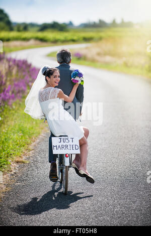 Ein Brautpaar nimmt die Straße auf einem Fahrrad. Sie haben Spaß für ihre Flitterwochen Stockfoto