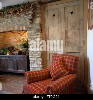 Rot aktiviert Sessel vor Kiefer Schranktüren im Wohnzimmer Land mit einer geschnitzten Eichenholz Truhe im Kamin aus Stein Stockfoto