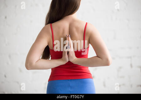 Schöne junge Frau in leuchtend bunte Sportbekleidung Training drinnen im Loft Interieur. Mädchen hält Anjali Mudra hinter Stockfoto