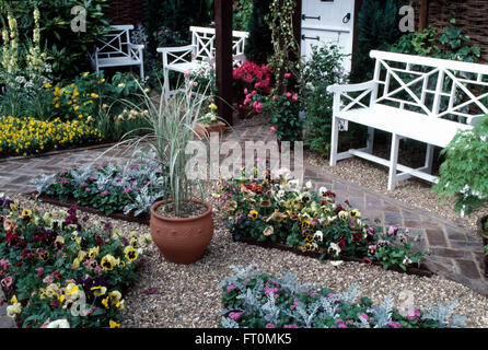 Bunte Stiefmütterchen in dreieckigen Betten im Hofgarten mit weißen Bänken auf Terrasse und hohen Gräsern in einem Terrakotta-Topf Stockfoto