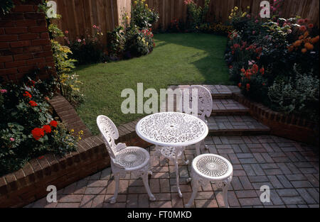 Weiße schmiedeeisernen Stühlen auf einer gepflasterten Terrasse in einem neu angelegte Garten mit gemauerten Stufen bis zu einer kleinen Wiese Stockfoto
