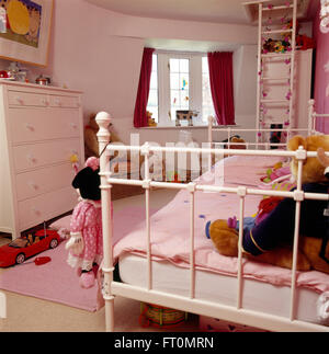 Weiß lackiertes Metall Bett mit rosa Decke im Kinderzimmer mit einer weißen Leiter gegen die Wand und eine weiße Kommode Stockfoto