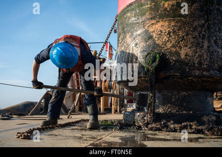 Seaman Chance Johnson, eine Boje Deck Crewmitglied an Bord der Coast Guard Cutter Katherine Walker, schabt Seepocken und marine Bewuchs aus einer Boje auf dem Deck von der Coast Guard Cutter Katherine Walker im Gange in den Hafen von New York, 8. März 2016. Katherine Walkers primäre Aufgabe ist die Aufrechterhaltung über 300 schwimmende Hilfsmittel zur Navigation in & rund um den Hafen von New York & seine Ansätze, Long Island Sound, der Hudson & East River & anderen Gewässern entlang der Küste von Connecticut, New York & New Jersey. (Foto: U.S. Coast Guard Petty Officer 3rd Class Frank Iannazzo-Simmons) Stockfoto