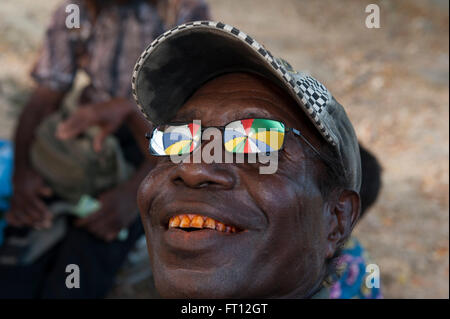 Reflexion von einem bunten Regenschirm in der Sonnenbrille eines Mannes mit roten Zähnen aus kauen Betelnuss, Wewak, Provinz Ost Sepik, Papua Neu Guinea, Süd-Pazifik Stockfoto