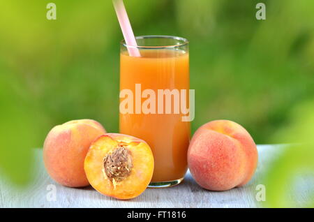 Glas köstliche Pfirsichsaft und Pfirsiche auf Tisch im Garten Stockfoto