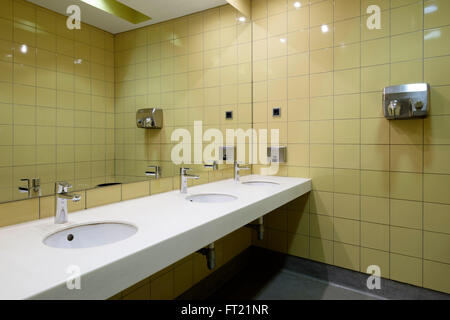 Öffentliche Toilette mit einer Reihe von Toiletten vor einem großen Spiegel Stockfoto