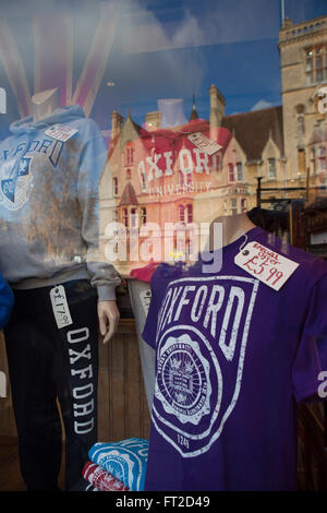 Eine Ladenfront in der Kommunalfinanzen Oxford, UK Verkauf Souvenier t-Shirts, sweat Tops und touristischen Aktivitäten mit der Reflexion an einer der Universitäten in das Fenster. Stockfoto