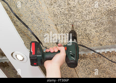 Schraubenzieher fährt Schrauben in der Decke von Faserplatten in einer hand Stockfoto