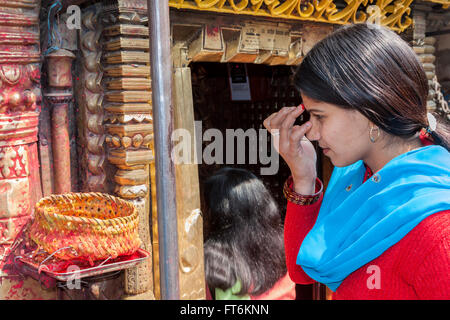 Nepal, Kathmandu.  Hindu Frau Anwendung Bindi von Kumkuma Pulver Stirn vor Eingabe Ashok Binayak (Maru Ganesh) Tempel. Stockfoto