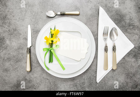 Frühling Tischdekoration mit Narzisse Blumen. Weißen Teller, Gabel, Messer auf graue Steinplatte Stockfoto