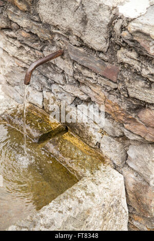 Nahaufnahme von Eisen Wasserhahn in Steinmauer im Freien mit fließendem Wasser im Reservoir mit Moos bedeckt Stockfoto